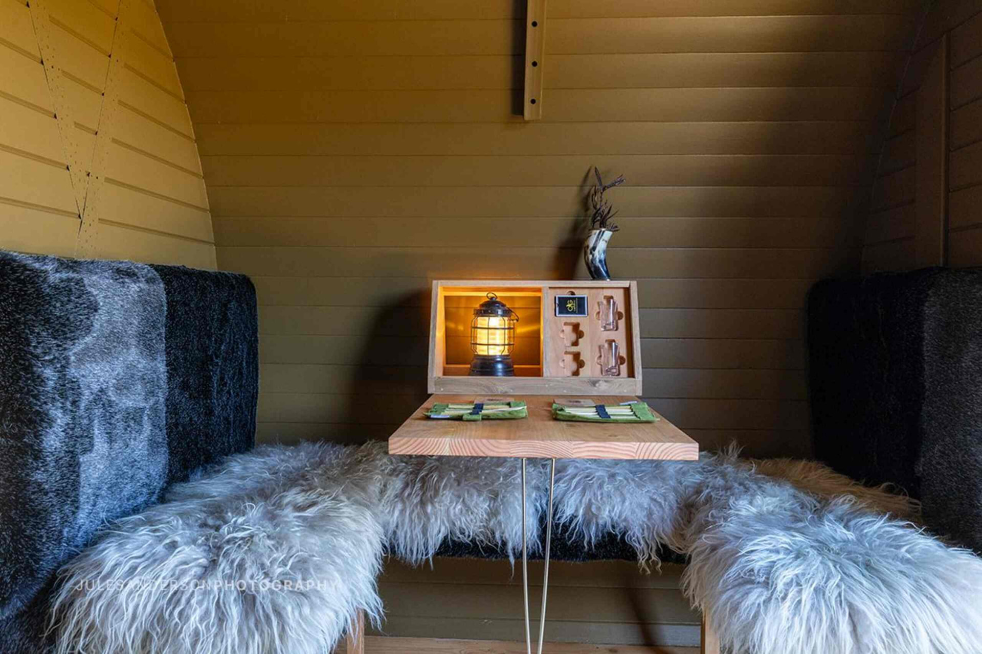 Cabin dining nook with sheepskin-covered bench seats, timber table and a lit lantern