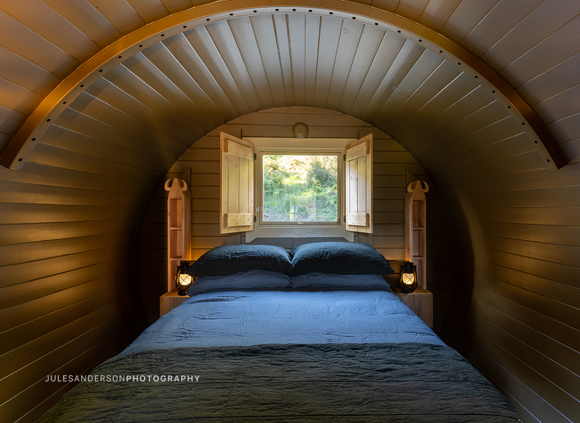 Warmly lit double bed inside the Balder barrel cabin with carved bedside shelves and lantern lighting